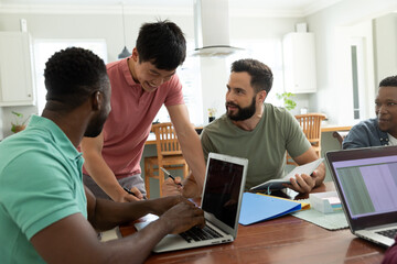 Smiling multiracial male entrepreneur talking with colleagues working at desk in office