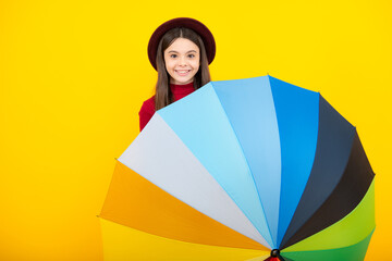 Obraz na płótnie Canvas Happy teenager portrait. Autumn kids concept. Child teenager girl covered face under rainbow umbrella in autumn hat on yellow studio background. Smiling girl.