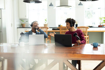 Multiracial young male workers wearing headphones and talking while recording podcast in office