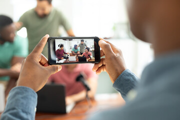 Hands of man with mobile phone filming multiracial male coworkers recording podcast in office
