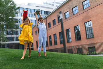 Obraz premium Two girls holding skateboards over their heads in city park, active kids concept.