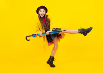 Child teenager girl with umbrella in autumn black leather skirt boots and hat isolated on yellow studio background. Excited teenager, glad amazed and overjoyed emotions.