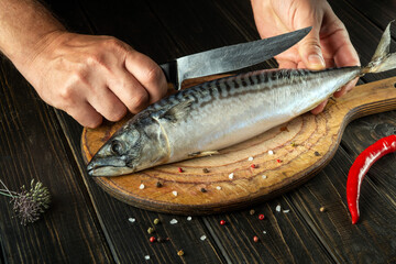 The chef cuts mackerel with a knife on the kitchen cutting board before cooking with spices. Menu for a restaurant or hotel