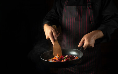 Cooking vegetables in a frying pan in the hands of a chef for a vegetarian food. Advertising space on a black background.
