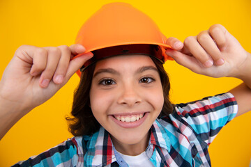 Close up portrait of child builder in helmet. Teenage girl on repairing work isolated on yellow background. Kids renovation concept.
