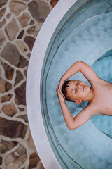 Top view of little boy relaxing with eyes closed in hot tub. Summer holiday, vacation concept.