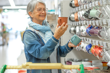 Portrait of smiling senior woman making purchases in the supermarket choosing a ceramic mug ...