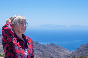 Naklejka premium Cheerful elderly woman enjoying the vacation expressing joy and freedom, in the background the mountains of Tenerife and the atlantic ocean