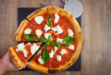 Female hand holds a slice of Italian pizza Margherita with tomato and buffalo mozzarella, pizza topped with fresh basil on the background on black board