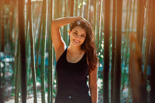 Young Latina woman smiling at the camera, in front of bamboo and sunlight coming form the background