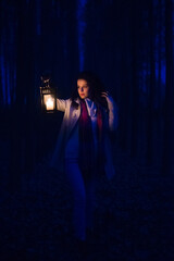 Young woman in the woods walking with lantern at night