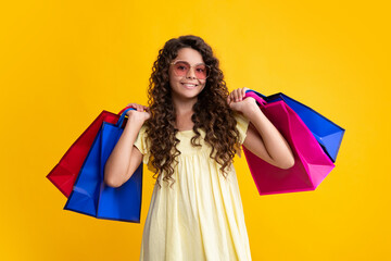 Beautiful fashion teenager child girl with shopping bags on yellow background. Shopaholic shopping...