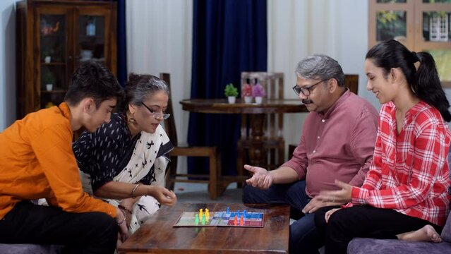 An old Indian couple and their children playing a board game - a childhood game  happy nuclear family  retired parents. Young kids spending quality time with their parents - two generations  leisur...