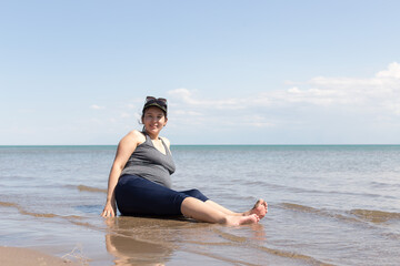 Fototapeta na wymiar Happy pregnant woman on sea vacation. Expectant mother sits on the sand against the background of the sea