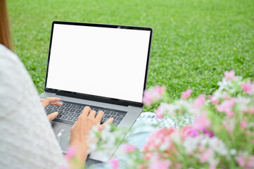 A young Asian female or college student sits under the tree in the park using her laptop.
