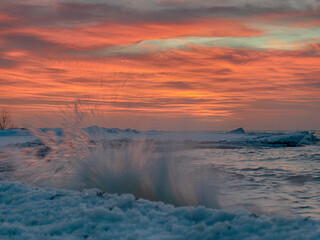 winter landscape from the sea shore, blurred wave slags against frozen ice cubes, blurred sunset color background