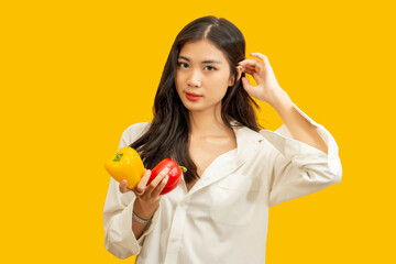 Vegetarian concept, Healthy woman holding colorful bell pepper on isolated yellow background