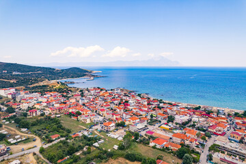 Naklejka na ściany i meble Aerial drone view of Greek seashore filled with whitewashed houses with vivid orange tiles. Nearly cloudless weather, sunshine, and blue sky. High quality photo