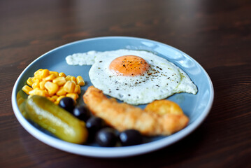 Beautiful breakfast in a blue plate on a wood table. Fried eggs with spices and cheese. Beautiful breakfast service. Chicken nuggets, olives, pickles on a plate. Fish sticks in batter. selective focus