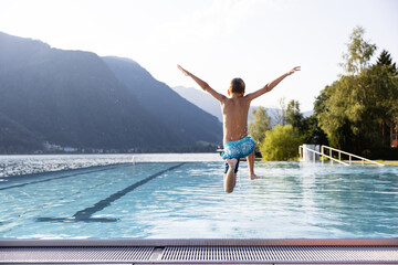 Active teenager boy jumping into an outdoor pool in the Alps. Summer holiday concept