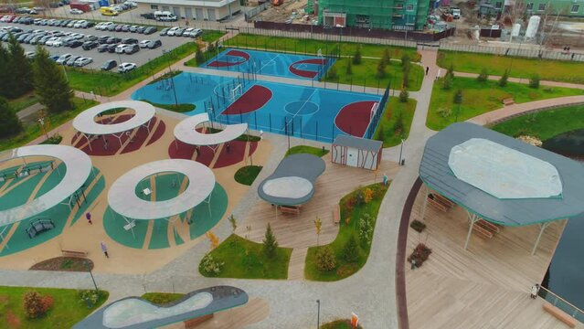 Children playground with roofs and sports fields on bank of pond in city park aerial view. Contemporary place for recreation
