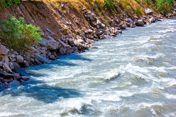 Fast mountain river water stream with waves flowing near the rocky shore in summer.