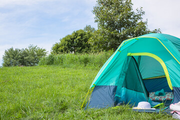 Bright colored camping tent in the lush, green meadow under a blue sky