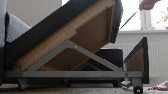 A man pulls out a pull-out double sofa bed for sleeping at home.