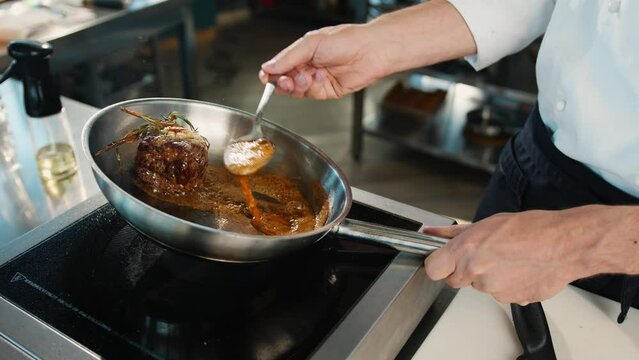 Close-up: Chef pouring sauce over filet mignon while cooking