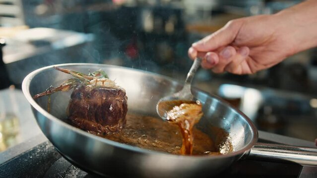 Close-up: Chef pouring sauce over filet mignon while cooking
