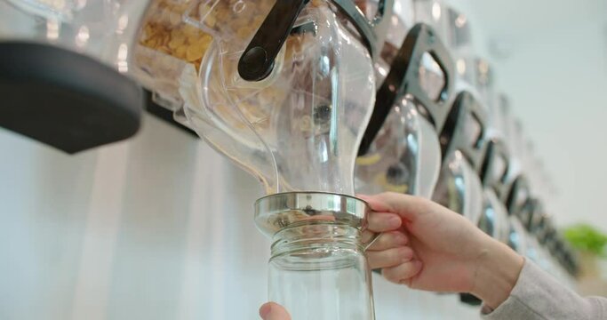 Closeup man pours bio organic product from vending machine to glass jar in zero waste shop. Customer buying food in plastic free grocery store. Eco friendly business. Reduce Reuse Recycle. Slow motion