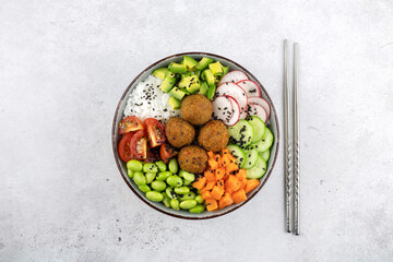 Poke bowl with rice, falafel, avocado, cherry tomatoes, green beans, cucumbers, sesame. Vegan poke bowl. Buddha bowl with rice, falafel, vegetables on a gray background, top view.