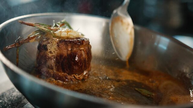 Close-up: Chef pouring sauce over filet mignon while cooking