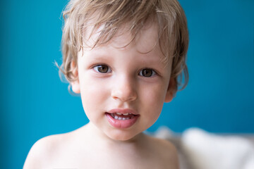 Portrait of little toddler boy looking at a camera sitting at home against blue background