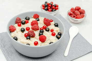 Oatmeal porridge with summer raspberry, currant berries. Porridge oats in bowl with fruits. Healthy food breakfast,lifestyle,dieting, proper nutrition. Top view flat lay on gray table background