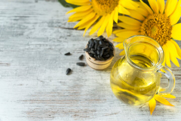 Sunflower oil in a glass jar, wooden bowl with seeds and two yellow sunflowers on the rustic...
