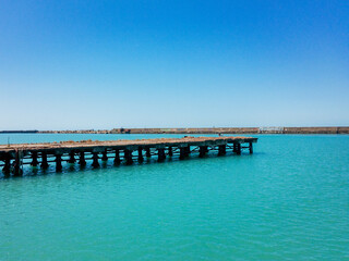 An old pier in turquoise sea water under a blue cloudless sky.