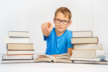 A happy smart kid with a lot of books is pointing at the camera. Successful in school concept.