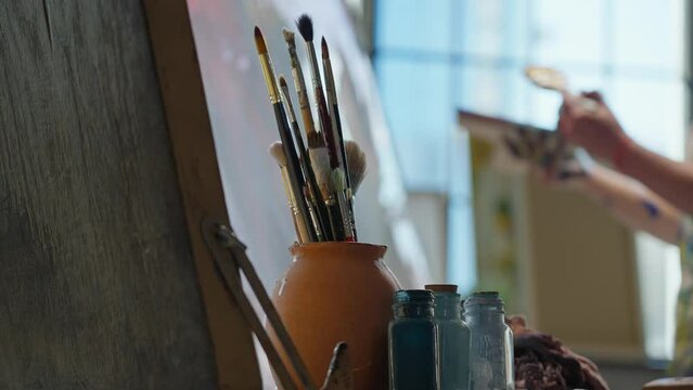 The artist's tools are brushes, paints, palette, canvas, easel, oil painting in a creative workshop. Blurred outlines of an artist creating a picture on canvas.