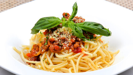 close-up spaghetti noodles topped with pieces of meat mixed with cheese and green vegetables served on a white plate