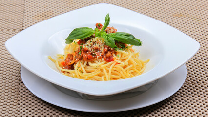 close-up spaghetti noodles topped with pieces of meat mixed with cheese and green vegetables served on a white plate