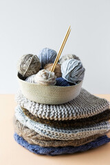 Gray, brown and blue balls of knitting threads in a beige basket with bamboo knitting needles and a...