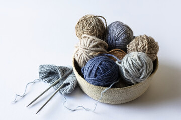 Fototapeta na wymiar Gray and blue balls of thread in a beige basket with knitting needles for knitting warm clothes, knitting hobby