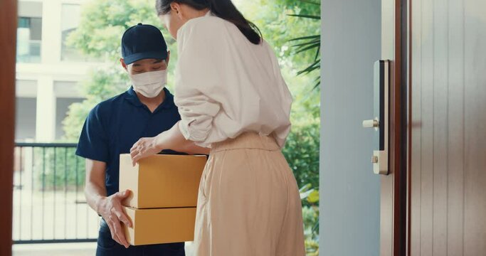 Young Asian delivery man wear mask in blue navy uniform carry case box knock door home online shopping cardboard box to woman in front of door lady scan QR code payment on smartphone at house concept.
