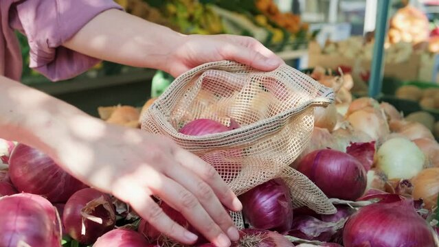 Woman at farmer market picking vegetables into knitted eco bag, close up side view.