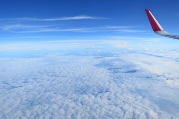 Beautiful view from airplane's window with airplane's wing, blue sky and white cloud in the summer morning. Soft focus. Transportation and nature concept.