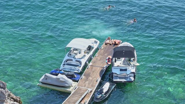 View from above on the motor boats moored to the wooden piers on which tourists from different countries rest and swim in the blue sea in the resort country.