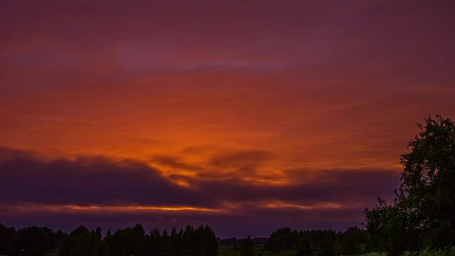 Low angle shot over red sunset sky with dark cloud movement in timelapse. Dark red sunlight sky over rural landscape.