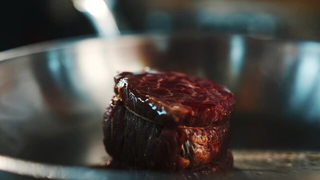 Close-up of a raw filet mignon being cooked in a frying pan