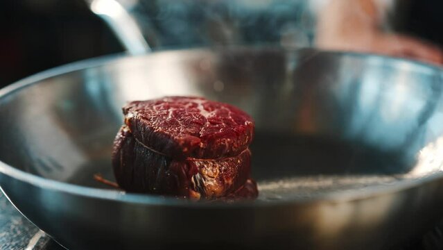 Close-up of a raw filet mignon being cooked in a frying pan